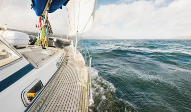 Teknelerle donatılmış modern bir yat. Tahta meşe güverteli. Clyde Nehri Firth 'ün kayalık kıyılarına doğru yol alıyorlar. Dramatik bir gökyüzü. İskoçya, İngiltere. Seyahat yerleri, eko turizm, tatiller, saf doğa.