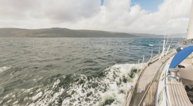 Teknelerle donatılmış modern bir yat. Tahta meşe güverteli. Clyde Nehri Firth 'ün kayalık kıyılarına doğru yol alıyorlar. Dramatik bir gökyüzü. İskoçya, İngiltere. Seyahat yerleri, eko turizm, tatiller, saf doğa.