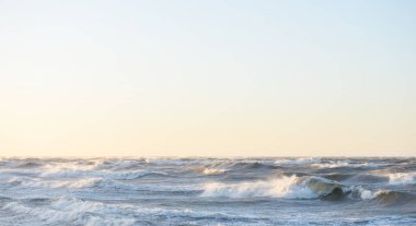Gün batımında Baltık kıyısı. Yumuşak altın güneş ışığı, parlayan gökyüzü, dalgalar. Idyllic deniz manzarası. Seyahat yerleri, eko turizm, doğa, hava durumu, iklim değişikliği. Resimli panoramik manzara