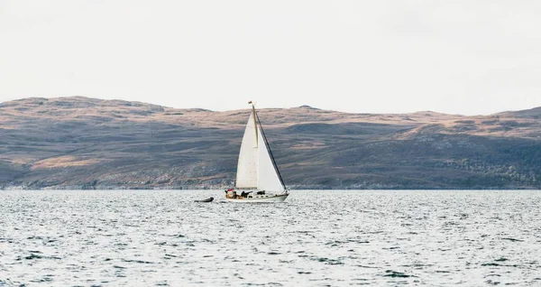 White yacht sailing near the rocky shores (cliffs) of the west coast of Jura island, a view from the yacht. Dramatic clouds after the storm. Inner Hebrides, Scotland, UK. Atmospheric landscape