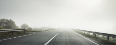 Gün doğumunda sisli bir havada boş otobanın arabasından ormana ve tarlalara doğru panoramik bir manzara. Avrupa. Ulaşım, lojistik, seyahat, yolculuk, özgürlük, sürüş. Kırsal alan