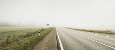 Gün doğumunda sisli bir havada boş otobanın arabasından ormana ve tarlalara doğru panoramik bir manzara. Avrupa. Ulaşım, lojistik, seyahat, yolculuk, özgürlük, sürüş. Kırsal alan