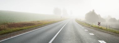 Gün doğumunda sisli bir havada boş otobanın arabasından ormana ve tarlalara doğru panoramik bir manzara. Avrupa. Ulaşım, lojistik, seyahat, yolculuk, özgürlük, sürüş. Kırsal alan