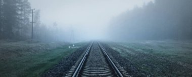 Kalın beyaz sisli tren yolu, arka planda orman. Manzara kavramı. Yük ve yolcu taşımacılığı, endüstri, iş, iletişim, çevresel hasar. Monokrom, gizem