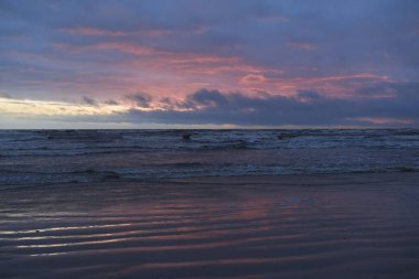 Fırtınadan sonra gün batımında Baltık Denizi. Dramatik gökyüzü, parlayan bulutlar, dofty altın güneş ışığı, dalgalar, fışkıran su. Resimli panoramik manzara. Doğa, çevre, ekoloji