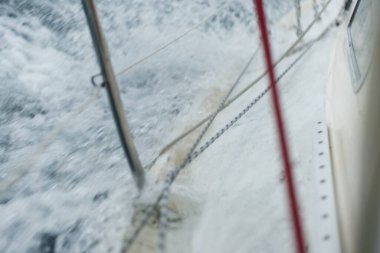 Açık denizde yelken açan topuklu bir yat. Güverte ve donanım görüntüsü. Karanlık fırtına dalgaları, su sıçramaları. Uzun pozlama, hareket. Kötü hava, kasırga, tehlike. Yarış, yarış, spor