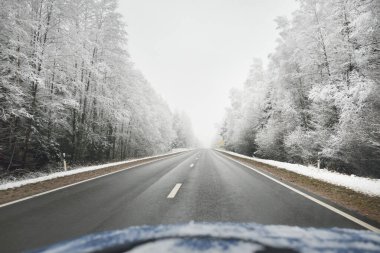 Boş otoyol (asfalt yol) karla kaplı ormanın içinden, kırsal alanda. Arabadan bak. Avrupa. Doğa, Noel tatilleri, uzak yerler, kış lastikleri, tehlikeli sürüş konsepti