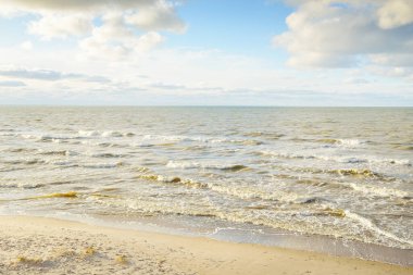 Kumlu bir sahilden (kum tepeleri) Baltık denizinin panoramik görüntüsü. Parlayan bulutlarla, dalgalarla ve su sıçramalarıyla berrak bir gökyüzü. Idyllic deniz manzarası. Sıcak kış havası, iklim değişikliği, doğa