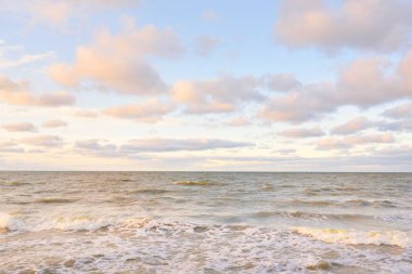 Gün batımında Baltık kıyıları (kum tepeleri). Yumuşak güneş ışığı, parlayan bulutlar, dalgalar ve su fışkıran berrak gökyüzü. Idyllic deniz manzarası. Liepaja, Letonya, Avrupa. Sıcak kış havası, iklim değişikliği, doğa