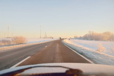 Karla kaplı orman ve kırsal alanda boş otoyol (asfalt yol). Gündoğumu, kar yağışı. Avrupa. Doğa, Noel tatilleri, uzak yerler, kış lastikleri, tehlikeli sürüş konsepti