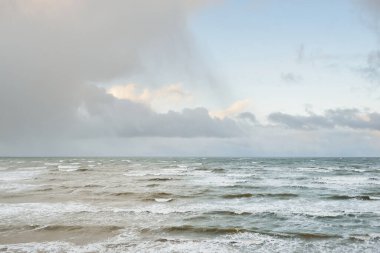 Fırtınadan sonra Baltık Denizi. Dramatik gökyüzü, parlayan bulutlar, yumuşak güneş ışığı. Dalgalar, su sıçratma. Resimli manzara, deniz manzarası, doğa. Panoramik görünüm