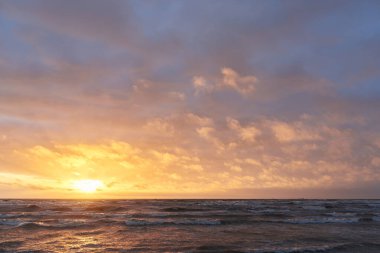 Fırtınadan sonra gün batımında Baltık Denizi. Dramatik gökyüzü, parlayan bulutlar, dofty altın güneş ışığı, dalgalar, fışkıran su. Resimli panoramik manzara. Doğa, çevre, ekoloji