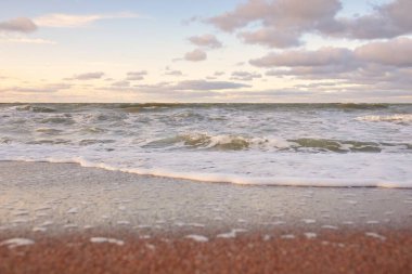 Gün batımında Baltık kıyıları (kum tepeleri). Yumuşak güneş ışığı, parlayan bulutlar, dalgalar ve su fışkıran berrak gökyüzü. Idyllic deniz manzarası. Liepaja, Letonya, Avrupa. Sıcak kış havası, iklim değişikliği, doğa