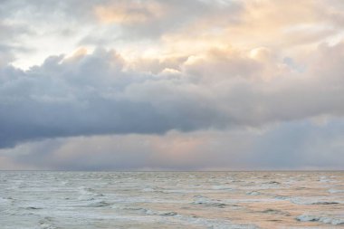 Fırtınadan sonra Baltık Denizi. Dramatik gökyüzü, parlayan bulutlar, yumuşak güneş ışığı. Dalgalar, su sıçratma. Resimli manzara, deniz manzarası, doğa. Panoramik görünüm