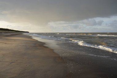 Gün batımında Baltık kıyıları (kum tepeleri). Yumuşak güneş ışığı, parlayan bulutlar, dalgalar ve su fışkıran berrak gökyüzü. Idyllic deniz manzarası. Liepaja, Letonya, Avrupa. Sıcak kış havası, iklim değişikliği, doğa