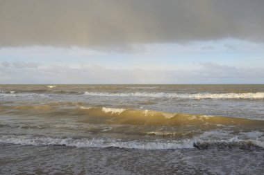 Kumlu bir sahilden (kum tepeleri) Baltık denizinin panoramik görüntüsü. Koyu bulutlu dramatik bir gökyüzü. Dalgalar, su sıçramaları. Idyllic deniz manzarası. Sıcak kış havası, iklim değişikliği, doğa. Danimarka