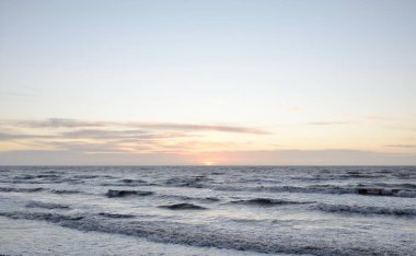 Gün batımında Baltık Denizi. Dramatik gökyüzü, mavi ve pembe parlayan bulutlar, altın güneş ışığı. Dalgalar, su sıçratma. Resimli manzara, deniz manzarası, doğa. Panoramik görünüm,