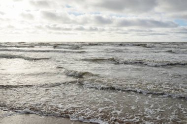 Fırtınadan sonra Baltık Denizi. Dramatik gökyüzü, parlayan bulutlar, yumuşak güneş ışığı. Dalgalar, su sıçratma. Resimli manzara, deniz manzarası, doğa. Panoramik görünüm
