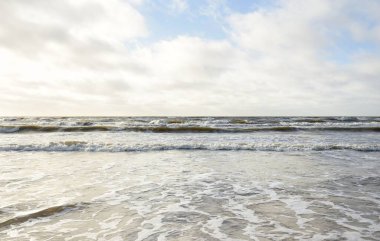 Kumlu sahilden Baltık denizinin panoramik görüntüsü (kum tepeleri). Parlak bulutlu dramatik bir gökyüzü. Dalgalar, su sıçramaları. Idyllic deniz manzarası. Bahar havası, iklim değişikliği, doğa