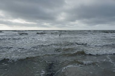 Kumlu sahilden Baltık Denizi manzarası (kum tepeleri). Dramatik gökyüzü, karanlık, parlak bulutlar. Dalgalar, su sıçramaları. Balıkçı tekneleri için eski iskele. Deniz Burnu. Bahar, iklim, doğa