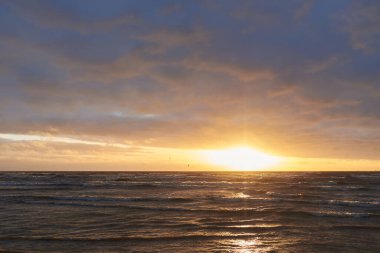 Fırtınadan sonra gün batımında Baltık Denizi. Dramatik gökyüzü, parlayan bulutlar, dofty altın güneş ışığı, dalgalar, fışkıran su. Resimli panoramik manzara. Doğa, çevre, ekoloji
