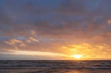 Fırtınadan sonra gün batımında Baltık Denizi. Dramatik gökyüzü, parlayan bulutlar, dofty altın güneş ışığı, dalgalar, fışkıran su. Resimli panoramik manzara. Doğa, çevre, ekoloji