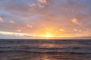 Fırtınadan sonra gün batımında Baltık Denizi. Dramatik gökyüzü, parlayan bulutlar, dofty altın güneş ışığı, dalgalar, fışkıran su. Resimli panoramik manzara. Doğa, çevre, ekoloji