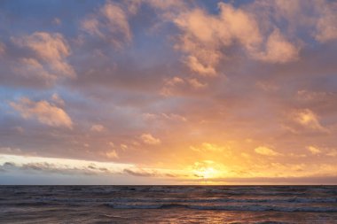 Fırtınadan sonra gün batımında Baltık Denizi. Dramatik gökyüzü, parlayan bulutlar, dofty altın güneş ışığı, dalgalar, fışkıran su. Resimli panoramik manzara. Doğa, çevre, ekoloji
