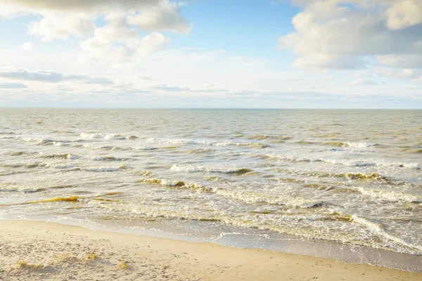 Kumlu bir sahilden (kum tepeleri) Baltık denizinin panoramik görüntüsü. Parlayan bulutlarla, dalgalarla ve su sıçramalarıyla berrak bir gökyüzü. Idyllic deniz manzarası. Sıcak kış havası, iklim değişikliği, doğa