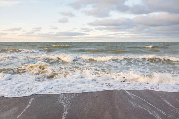Gün batımında Baltık kıyıları (kum tepeleri). Yumuşak güneş ışığı, parlayan bulutlar, dalgalar ve su fışkıran berrak gökyüzü. Idyllic deniz manzarası. Liepaja, Letonya, Avrupa. Sıcak kış havası, iklim değişikliği, doğa