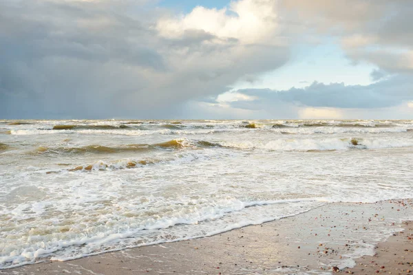 Fırtınadan sonra Baltık Denizi. Dramatik gökyüzü, parlayan bulutlar, yumuşak güneş ışığı. Dalgalar, su sıçratma. Resimli manzara, deniz manzarası, doğa. Panoramik görünüm