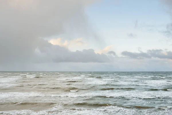 Fırtınadan sonra Baltık Denizi. Dramatik gökyüzü, parlayan bulutlar, yumuşak güneş ışığı. Dalgalar, su sıçratma. Resimli manzara, deniz manzarası, doğa. Panoramik görünüm