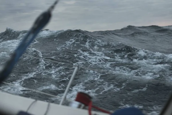 Açık denizde yelken açan topuklu bir yat. Kırmızı vinç ve donanım. Karanlık fırtına dalgaları, su sıçramaları. Uzun pozlama, hareket. Kötü hava, kasırga, tehlike. Yarış, yarış, spor