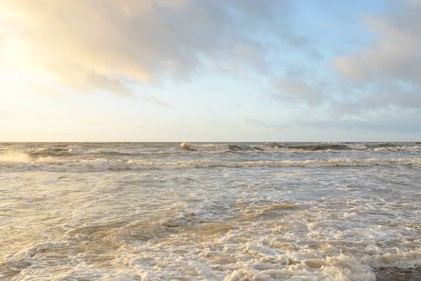 Gün batımında Baltık Denizi. Dramatik gökyüzü, mavi ve pembe parlayan bulutlar, altın güneş ışığı. Dalgalar, su sıçratma. Resimli manzara, deniz manzarası, doğa. Panoramik görünüm,