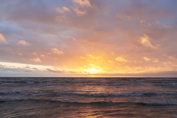 Fırtınadan sonra gün batımında Baltık Denizi. Dramatik gökyüzü, parlayan bulutlar, dofty altın güneş ışığı, dalgalar, fışkıran su. Resimli panoramik manzara. Doğa, çevre, ekoloji
