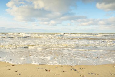 Kumlu bir sahilden (kum tepeleri) Baltık denizinin panoramik görüntüsü. Parlayan bulutlarla, dalgalarla ve su sıçramalarıyla berrak bir gökyüzü. Idyllic deniz manzarası. Sıcak kış havası, iklim değişikliği, doğa