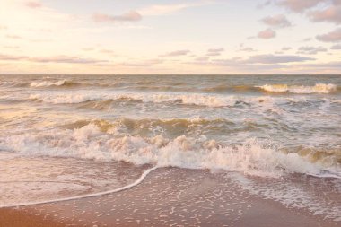 Gün batımında Baltık kıyıları (kum tepeleri). Yumuşak güneş ışığı, parlayan bulutlar, dalgalar ve su fışkıran berrak gökyüzü. Idyllic deniz manzarası. Liepaja, Letonya, Avrupa. Sıcak kış havası, iklim değişikliği, doğa