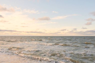 Gün batımında Baltık kıyıları (kum tepeleri). Yumuşak güneş ışığı, parlayan bulutlar, dalgalar ve su fışkıran berrak gökyüzü. Idyllic deniz manzarası. Liepaja, Letonya, Avrupa. Sıcak kış havası, iklim değişikliği, doğa