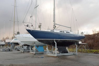 Mavi yelkenli donanımlı yelkenli bir yat kulübünde karada duruyor. Hizmet, onarım, ulaşım, spor, eğlence, eğlence aktivitesi