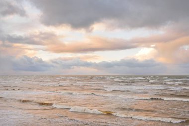 Fırtınadan sonra Baltık Denizi. Dramatik gökyüzü, parlayan bulutlar, yumuşak güneş ışığı. Dalgalar, su sıçratma. Resimli manzara, deniz manzarası, doğa. Panoramik görünüm