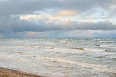 Fırtınadan sonra Baltık Denizi. Dramatik gökyüzü, parlayan bulutlar, yumuşak güneş ışığı. Dalgalar, su sıçratma. Resimli manzara, deniz manzarası, doğa. Panoramik görünüm