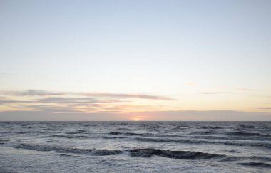 Gün batımında Baltık Denizi. Dramatik gökyüzü, mavi ve pembe parlayan bulutlar, altın güneş ışığı. Dalgalar, su sıçratma. Resimli manzara, deniz manzarası, doğa. Panoramik görünüm,