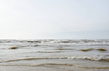 Gün batımında Baltık kıyısı. Yumuşak güneş ışığı, parlayan bulutlar, dalgalar ve su fışkıran berrak gökyüzü. Idyllic deniz manzarası. Hava, iklim değişikliği, doğa