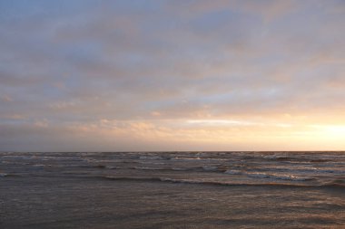 Fırtınadan sonra gün batımında Baltık Denizi. Dramatik gökyüzü, parlayan bulutlar, dofty altın güneş ışığı, dalgalar, fışkıran su. Resimli panoramik manzara. Doğa, çevre, ekoloji