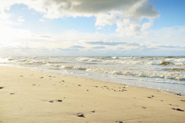 Kumlu bir sahilden (kum tepeleri) Baltık denizinin panoramik görüntüsü. Parlayan bulutlarla, dalgalarla ve su sıçramalarıyla berrak bir gökyüzü. Idyllic deniz manzarası. Sıcak kış havası, iklim değişikliği, doğa