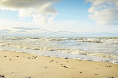 Kumlu bir sahilden (kum tepeleri) Baltık denizinin panoramik görüntüsü. Parlayan bulutlarla, dalgalarla ve su sıçramalarıyla berrak bir gökyüzü. Idyllic deniz manzarası. Sıcak kış havası, iklim değişikliği, doğa