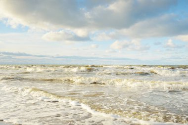 Kumlu bir sahilden (kum tepeleri) Baltık denizinin panoramik görüntüsü. Parlayan bulutlarla, dalgalarla ve su sıçramalarıyla berrak bir gökyüzü. Idyllic deniz manzarası. Sıcak kış havası, iklim değişikliği, doğa