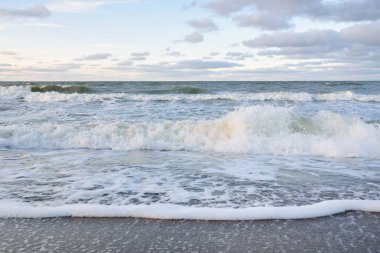 Gün batımında Baltık kıyıları (kum tepeleri). Yumuşak güneş ışığı, parlayan bulutlar, dalgalar ve su fışkıran berrak gökyüzü. Idyllic deniz manzarası. Liepaja, Letonya, Avrupa. Sıcak kış havası, iklim değişikliği, doğa