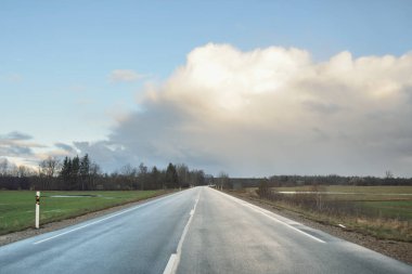 Gün batımında tarla ve orman boyunca asfalt yol (karayolu). Arabadan görüntü. Turizm, tatiller, uzak yerler, lojistik kavramlar