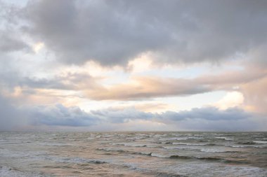 Fırtınadan sonra Baltık Denizi. Dramatik gökyüzü, parlayan bulutlar, yumuşak güneş ışığı. Dalgalar, su sıçratma. Resimli manzara, deniz manzarası, doğa. Panoramik görünüm